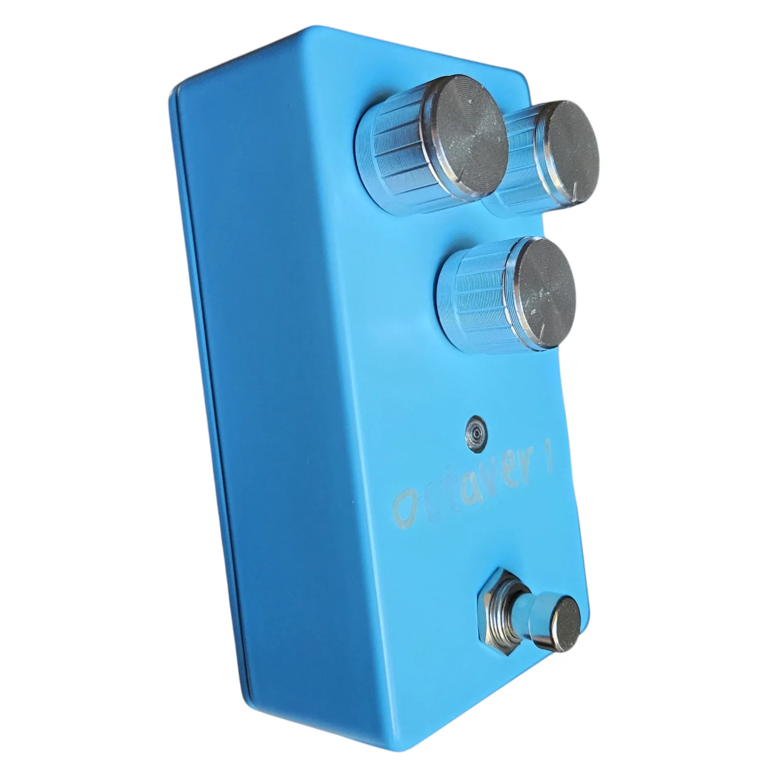 The blue box at a three-quarter angle from the left, the three silver knobs standing off the face, the LED and the footswitch below, and the long plain side of the box on the left.