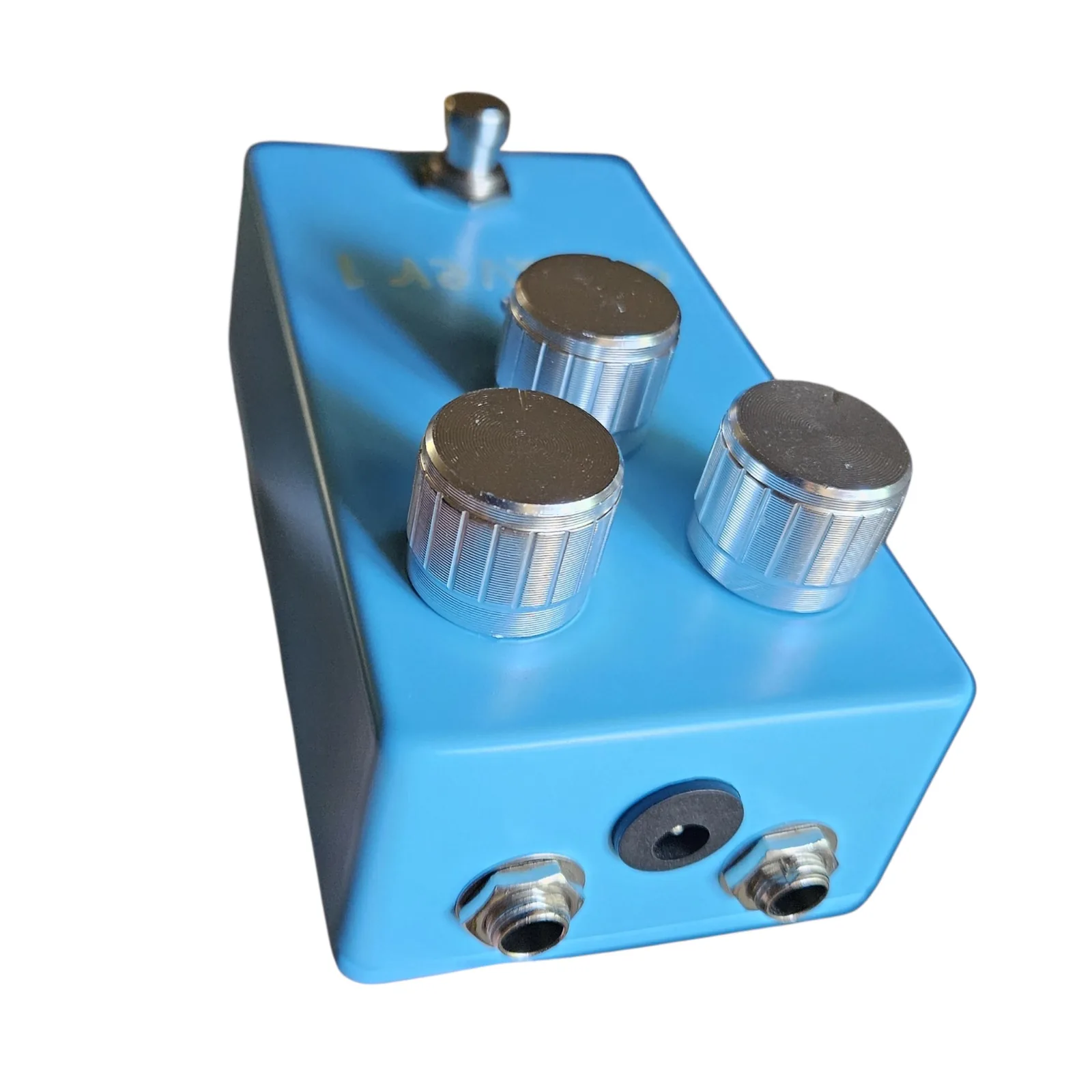 The blue box from above its top end, showing three jacks in the top edge, a barrel power jack in the middle between two quarter-inch sockets, with the three silver knobs and the footswitch standing up from the face beyond.
