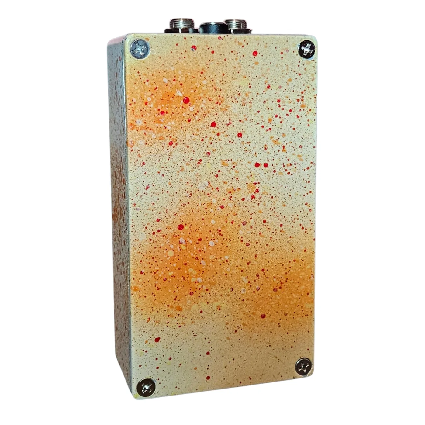 Back of the pedal: the bottom plate is cream misted with orange and spattered with fine red dots, with a Phillips screw in each corner and no label. The jacks and DC socket show along the top edge.