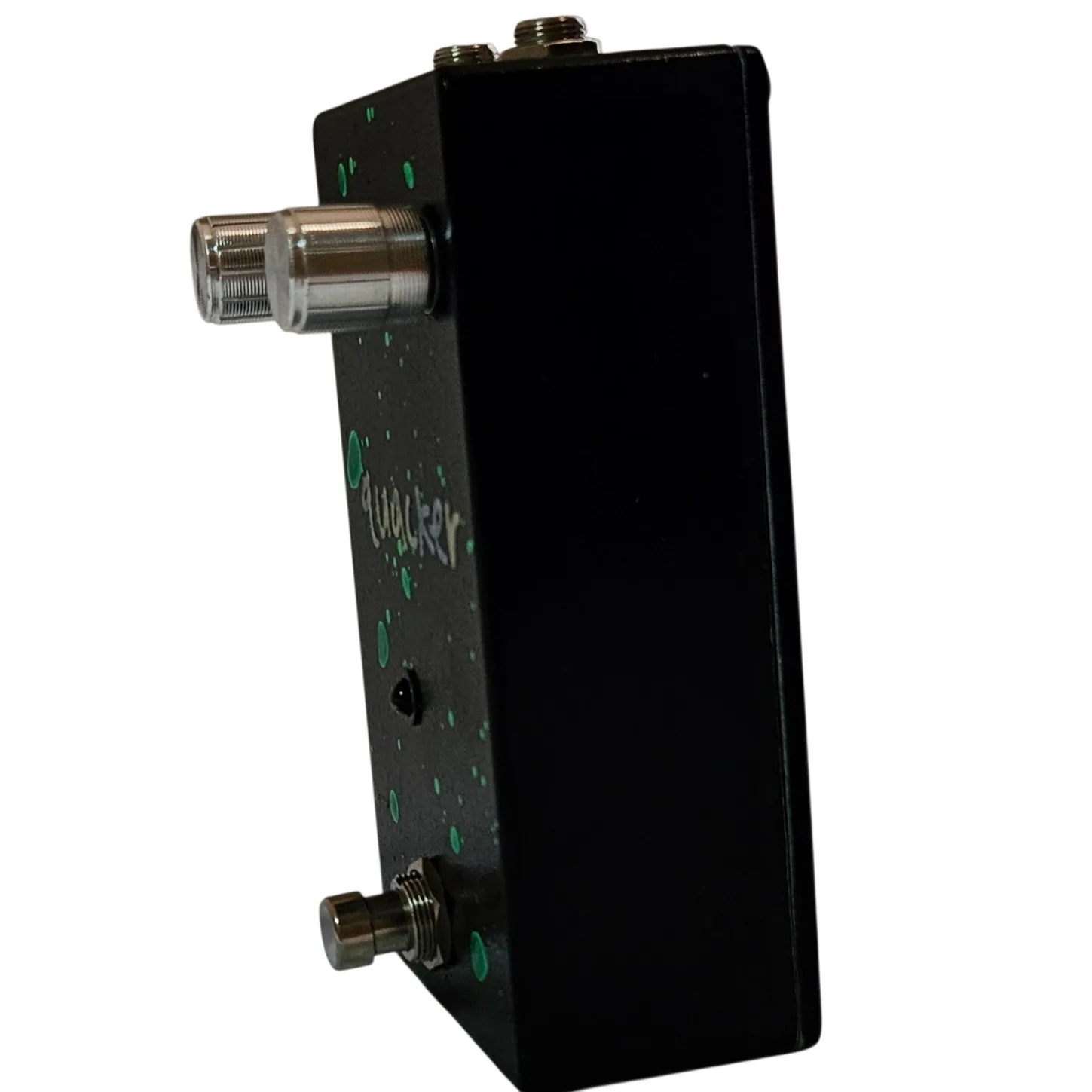 The pedal from the other three-quarter angle, a chrome knob catching the light at the top and the green spatters scattered across the black face and flank.
