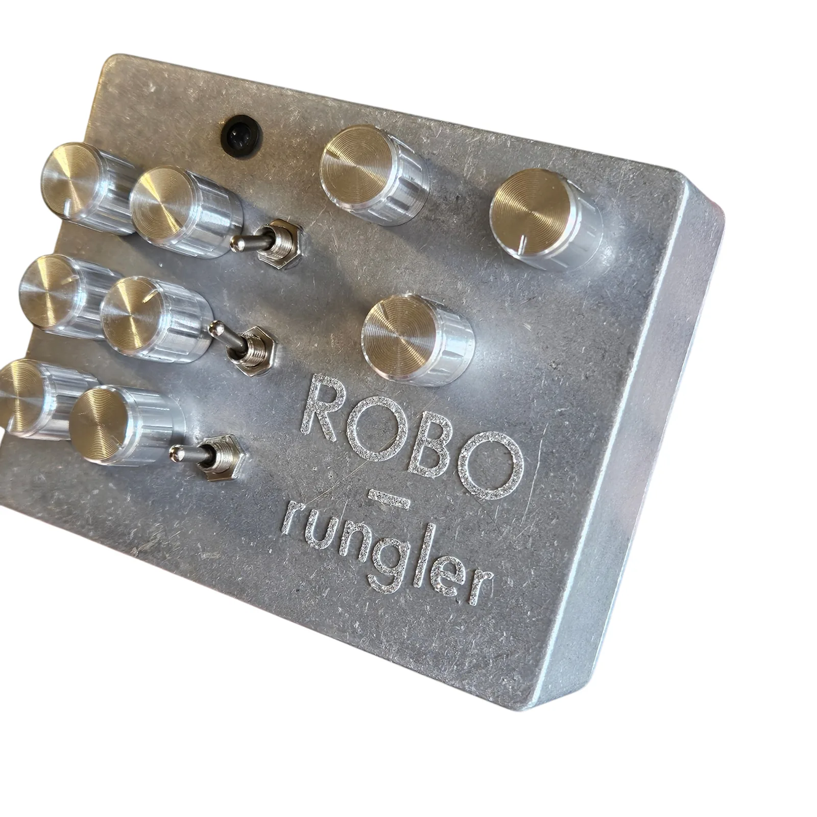 The face of a raw aluminum box seen close at an angle, ROBO and rungler engraved in the lower right. Six ribbed silver knobs in three pairs run down the left with a chrome toggle beside each pair, three more knobs sit at the upper right, and a small dark LED is near the top.