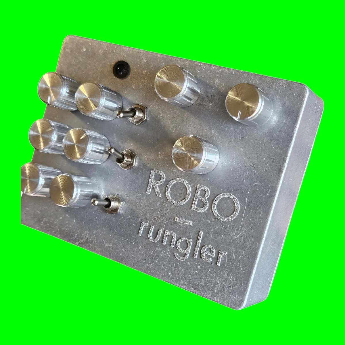 The face of a raw aluminum box seen close at an angle, ROBO and rungler engraved in the lower right. Six ribbed silver knobs in three pairs run down the left with a chrome toggle beside each pair, three more knobs sit at the upper right, and a small dark LED is near the top.