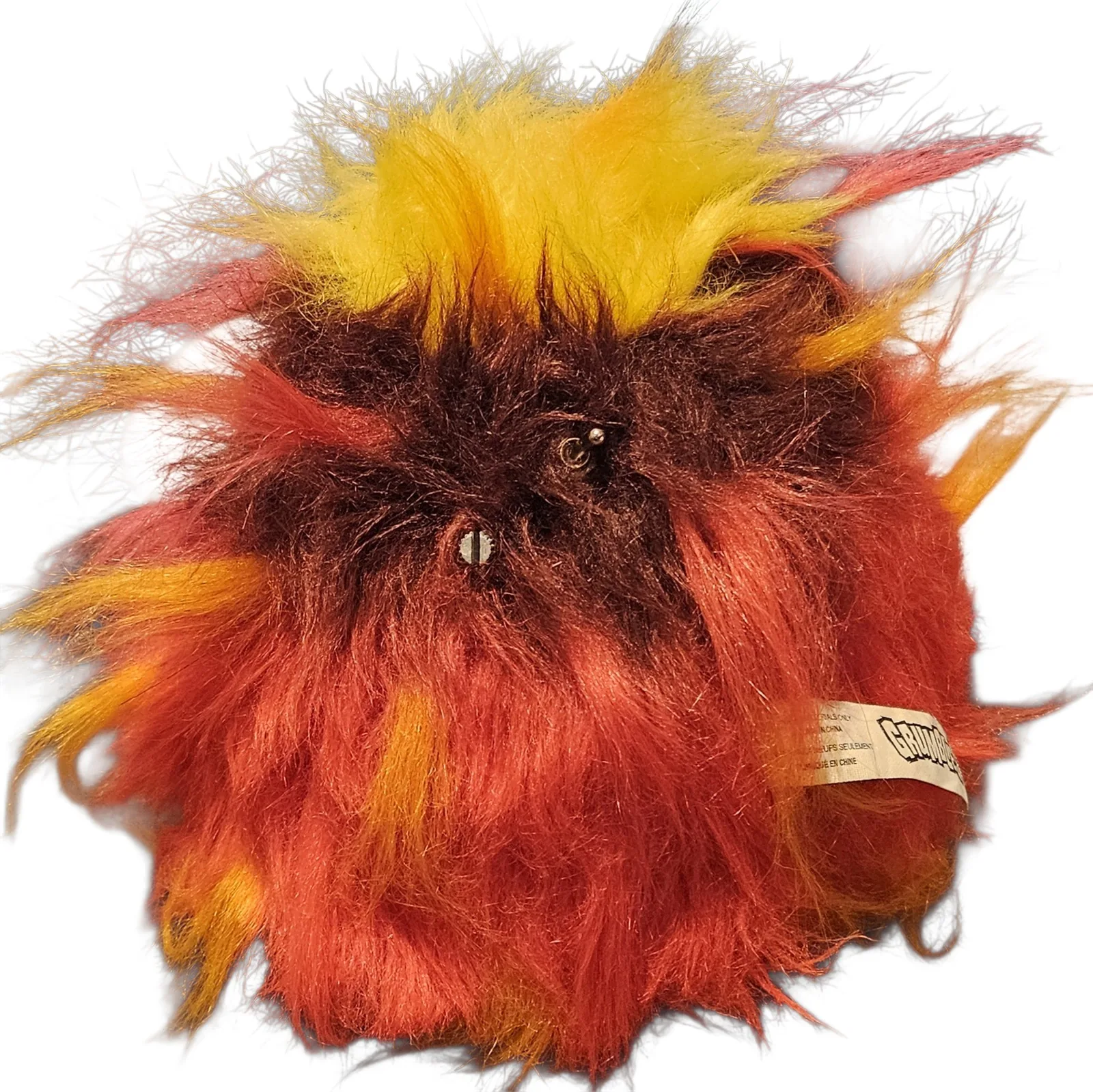 The back of the creature, a ball of the same fiery fur parted around two bare metal stems: the slotted volume-pot shaft and a small ball-top on/off toggle, mounted straight through the shell with no knobs on either. The original Grumblies fabric tag pokes out at the side.