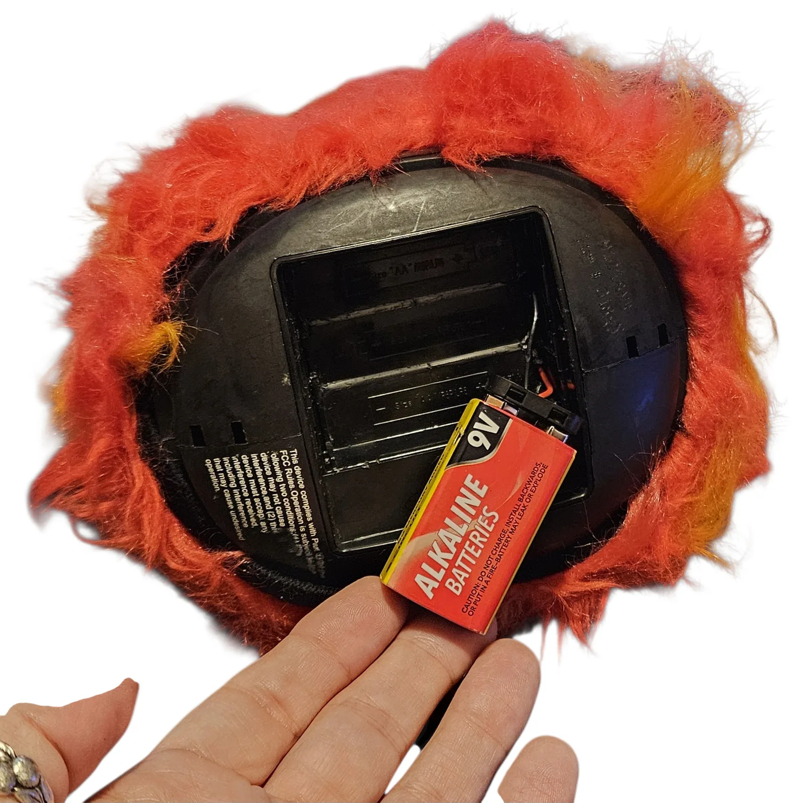 The underside held in one hand: a black plastic base with the battery door open and a 9V alkaline battery lying in the compartment where the AA cells used to go.