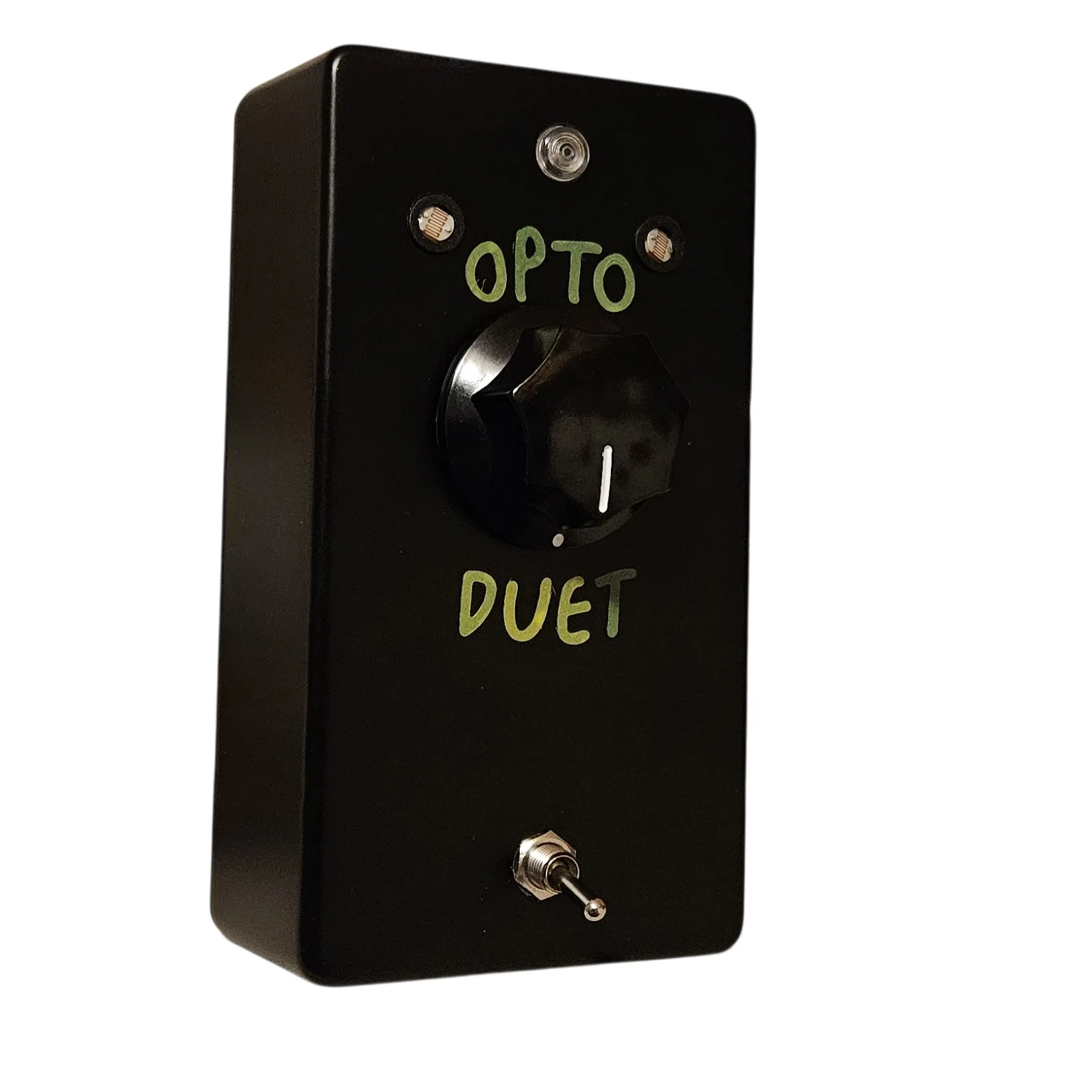 An upright black box photographed at a slight angle. A small unlit LED sits at the top center with a round mesh-faced window on either side of it. OPTO is hand-lettered below them in yellow-green capitals, a large black fluted knob with a white pointer line sits in the middle of the face, and DUET is lettered underneath in the same yellow-green. A small chrome toggle switch stands alone near the bottom.