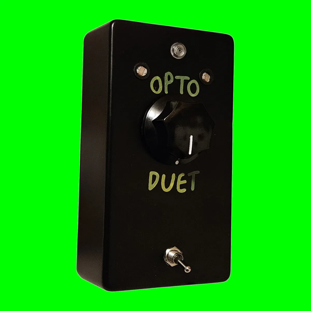 Solo Duet - an upright black box with a round mesh-faced photocell window either side of an unlit LED at the top, OPTO hand-lettered in yellow-green above a large black fluted knob, DUET lettered below it and a small chrome toggle near the bottom, on a chroma green tile