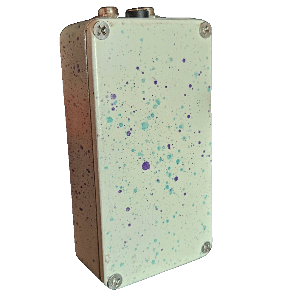 Back of the pedal: a cream bottom plate scattered with teal and purple splatter dots, with a Phillips screw in each corner and no label. Two jacks and the DC socket show along the top edge.
