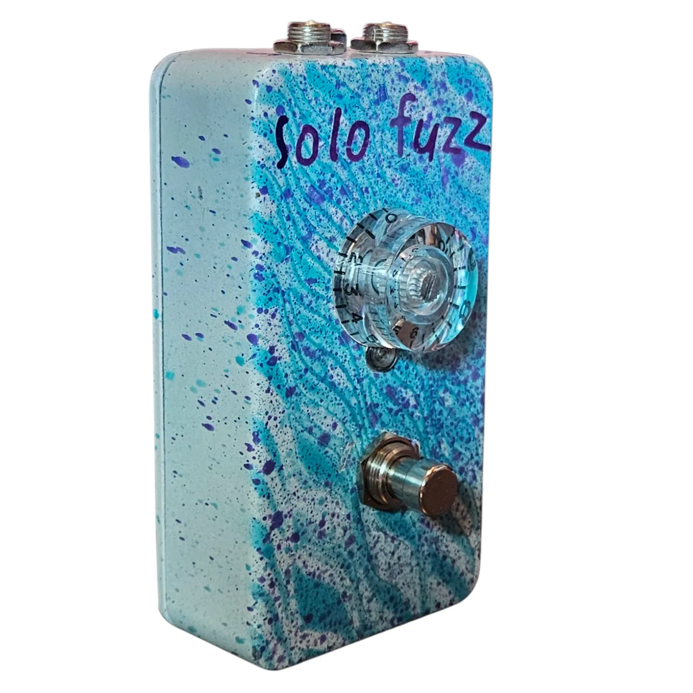 Left side of the pedal: a cream wall flecked with purple and teal, showing the clear knob - its skirt numbered around the edge up to 10 - standing off the face, with the footswitch below it on a white washer.