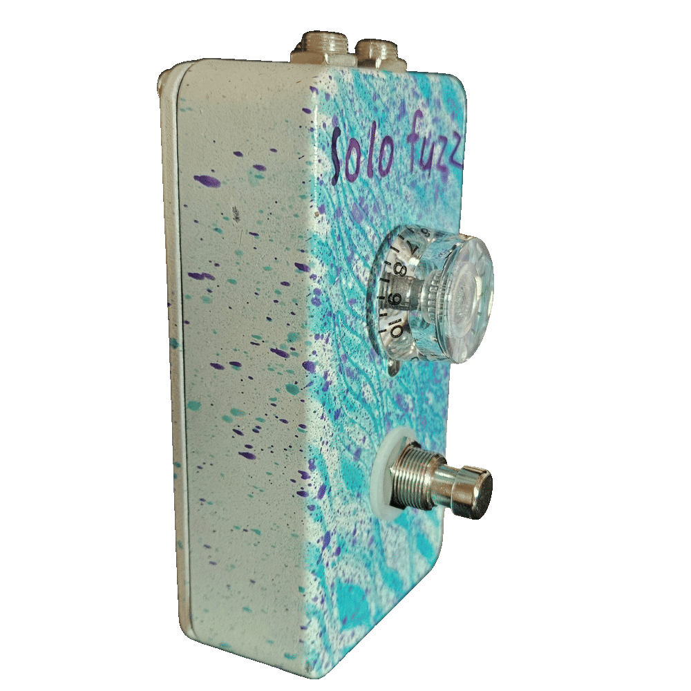 Left side of the pedal: a cream wall flecked with purple and teal, showing the clear knob &mdash; its skirt numbered around the edge up to 10 &mdash; standing off the face, with the footswitch below it on a white washer.