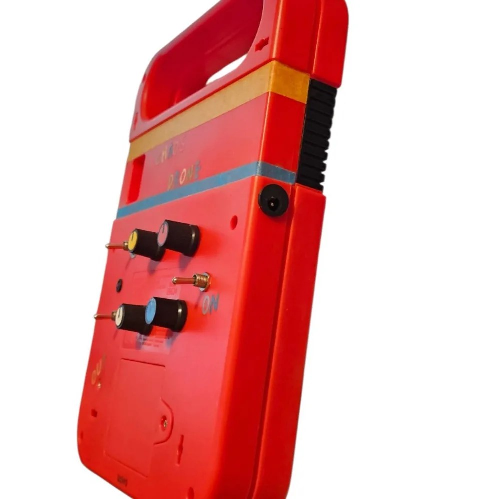 A close view of the side edge of the case, showing a black barrel charge socket set into the red plastic beside the toy's ribbed grip strip. Two of the panel knobs and the toggle labeled ON are visible around the corner on the back.