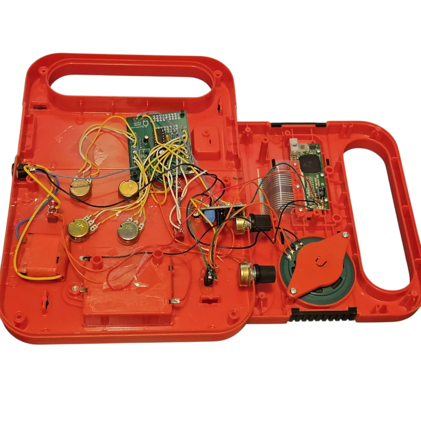 The red case opened flat and empty of its front panel. In the left half a green circuit board silkscreened Synthrotek NAND Synth sits at the top, wired with yellow, white, blue and black leads to four gold potentiometer bodies mounted through the case, a small board carrying a blue capacitor, and a red battery holder. In the right half are a green charge-controller board, a battery pack, a small amplifier board, two more potentiometers and the toy's original round green speaker held down by an orange plastic clamp.