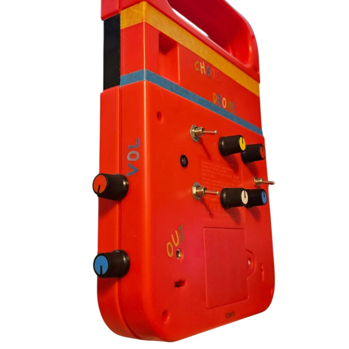 A close angled view of the back panel. VOL is spelled in blue sticker letters down the left edge above a black knob with an orange pointer, with a second knob below it. The four panel knobs and two of the toggles are at the right, the original Texas Instruments label is still on the case between them, and OUT is lettered beside its jack at the bottom.