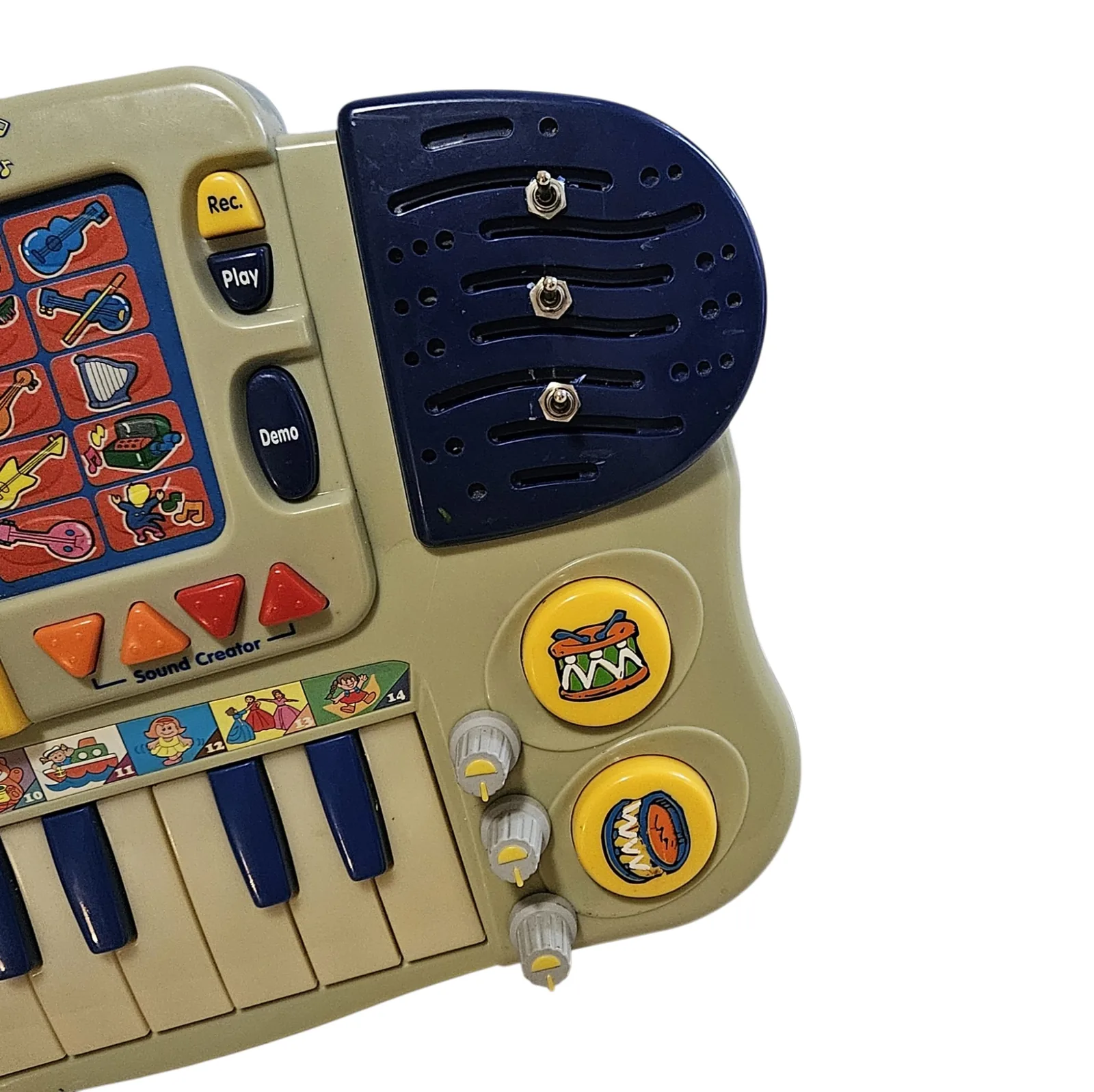 A close angled view of the right end. Three silver toggle switches are mounted straight through the dark blue speaker grille in a vertical row, and three small knurled gray knobs with yellow pointer marks run down the edge of the case below them, beside two round yellow drum pads. The Rec, Play and Demo buttons and the orange and red Sound Creator triangles are to the left.
