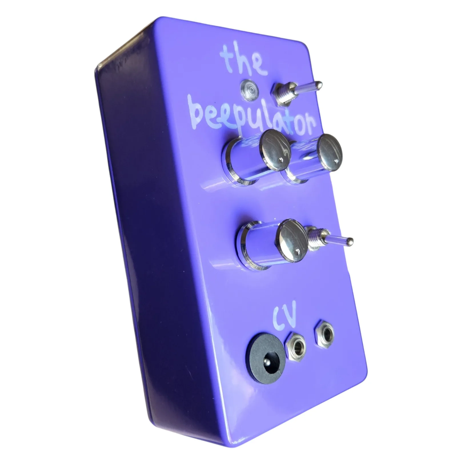 The purple box at a three-quarter angle from the left, the chrome knobs and the two toggles standing out from the face, the hand lettering and the three jacks at the bottom receding toward the far edge.