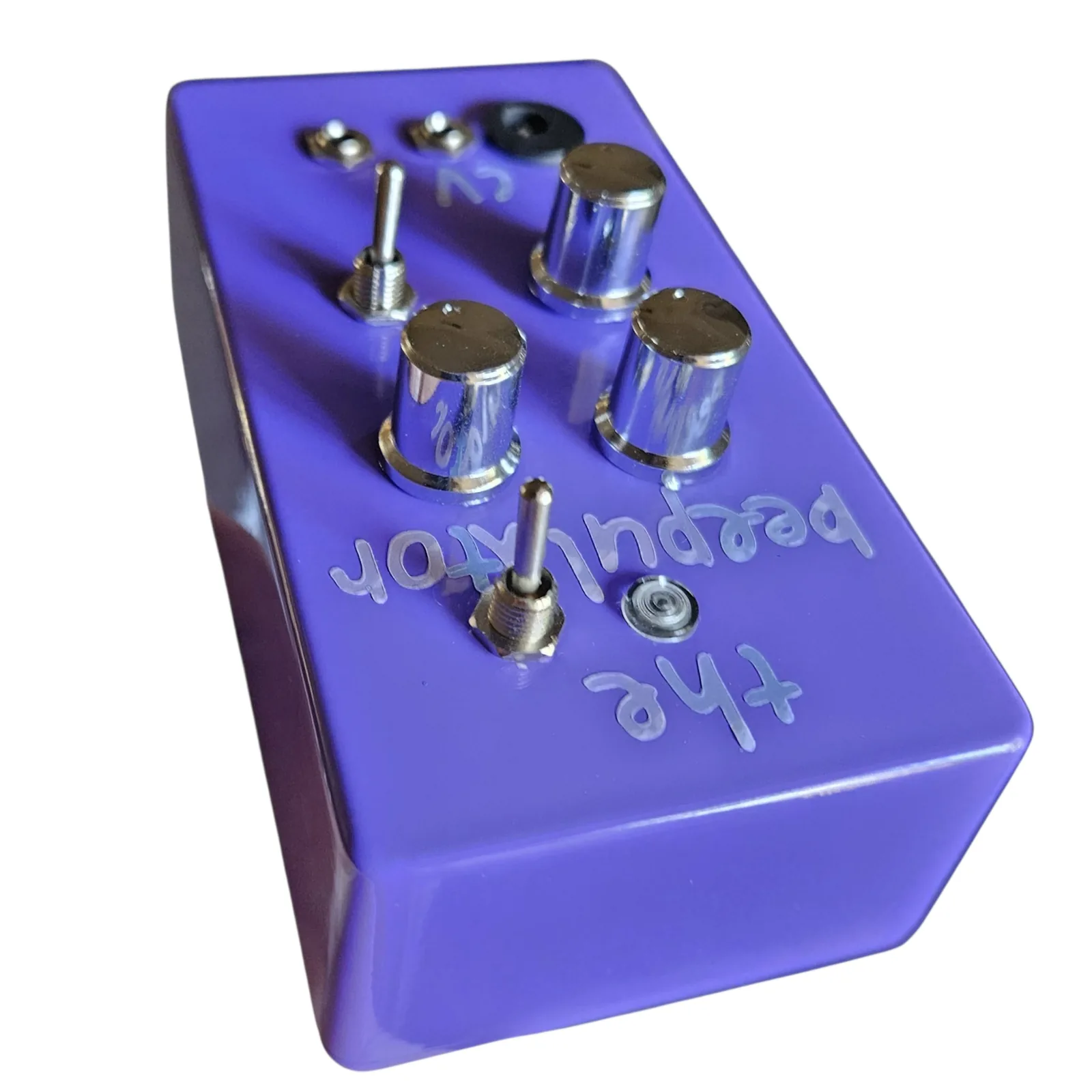 The purple box seen from above its top end, upside down, so the lettering reads the beepulator backwards across the face, the three chrome knobs and the toggles standing up in the middle and the LED near the edge.