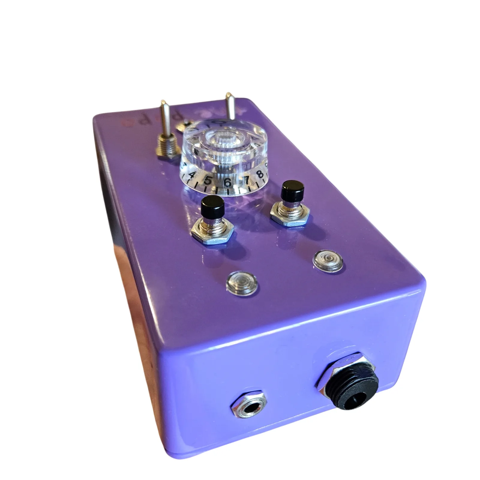 The box lying on its back, seen from its top end at a low angle: a small jack and a round black power socket on the top edge nearest the camera, with the two lights, the push buttons and the clear knob standing up beyond them.