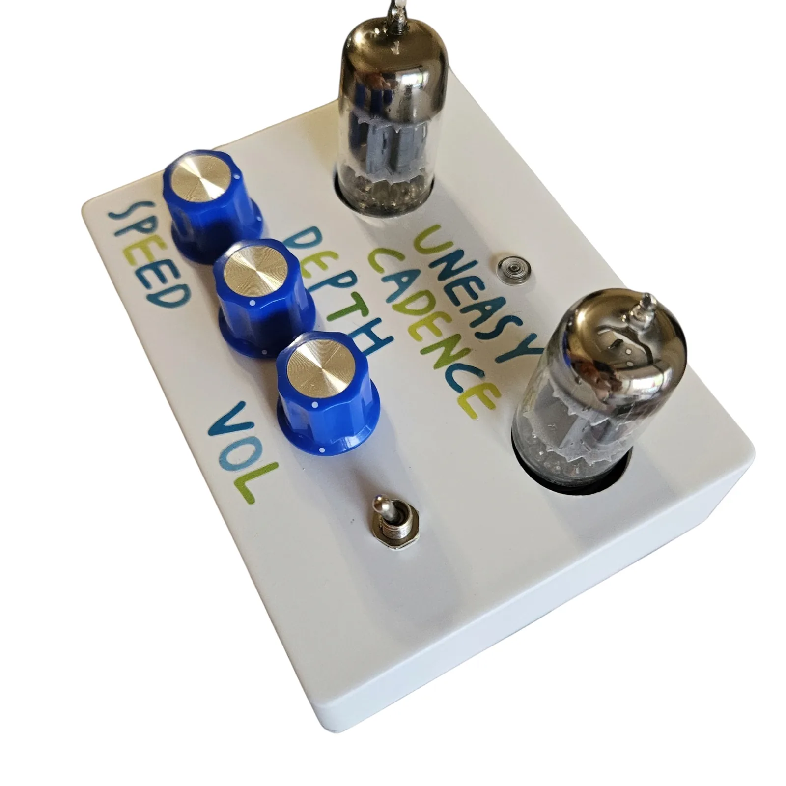 The box from its right side, looking along the face. The silver toggle is nearest with VOL lettered beside it, then the three blue knobs in a line with DEPTH and SPEED along the far edge. UNEASY CADENCE is lettered between the two tubes, with the indicator lamp beside it.
