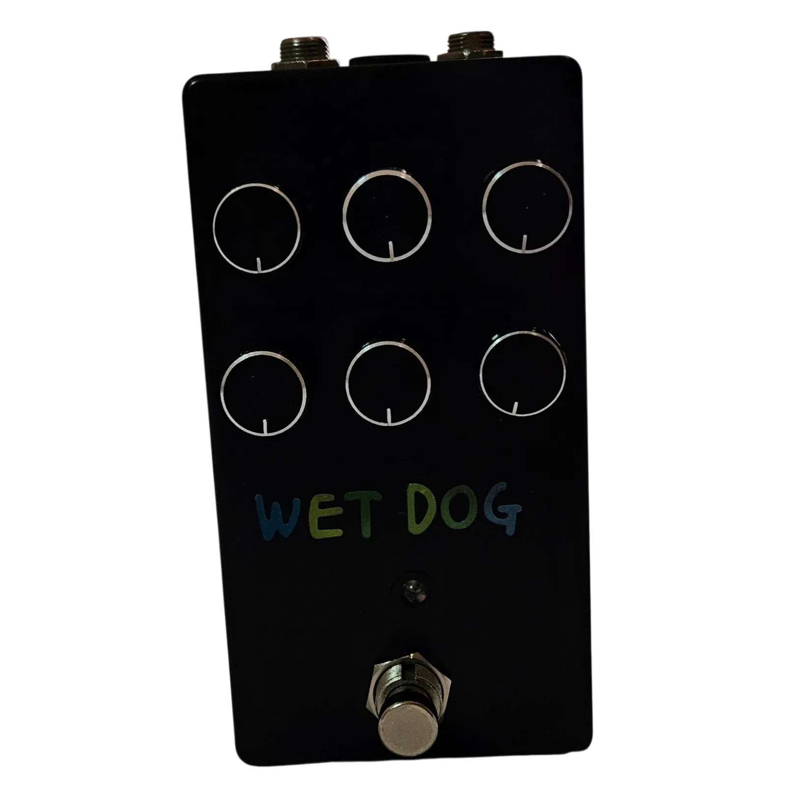 A tall black pedal photographed face on. Six black knobs with thin white pointer lines stand in two rows of three, each ringed by a thin painted circle. WET DOG is hand-lettered below them in blue and green capitals, with a small LED beneath and a silver footswitch at the bottom.